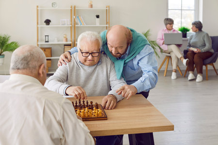 Group of a male elderly senior people playing chess in nursing home sitting at the table. Pensioners spending leisure time together playing board games. Leisure in retirement home concept.の写真素材