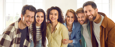 Group of happy smiling funny friends students or colleagues in casual clothes standing together and looking cheerful at camera. Portrait of friendly guys and girls hugging indoors. Banner.の写真素材