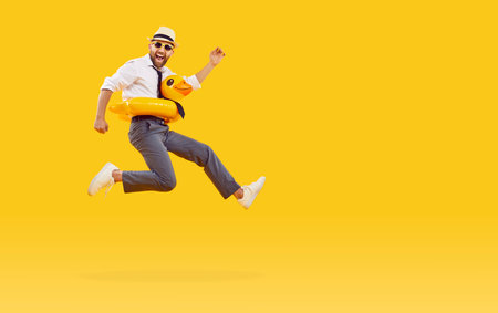 Funny happy man in office clothes, sunglasses and with duck rubber ring is going on summer holiday trip and having fun jumping on a yellow background with copy space. Vacation and travel concept.の写真素材