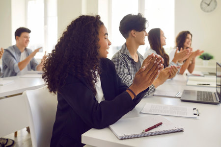 Group of a happy young diverse students applauding to lecturer or their teacher during a lesson at university classroom. Multiethnic high school people sitting at the desk and clapping hands.の写真素材