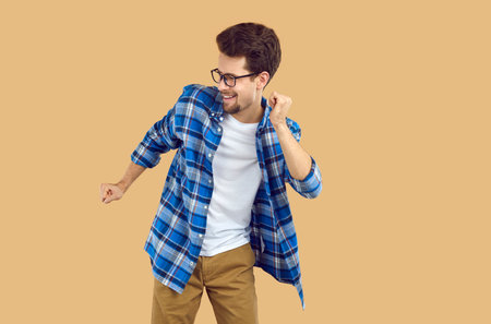 Happy young man dancing over isolated studio background. Portrait of overjoyed bearded man wearing glasses and blue plaid shirt having fun or celebrating successの写真素材