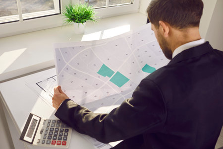 Male professional engineer analyzing cadastral map in office. Shoulder view shot of cartographer...