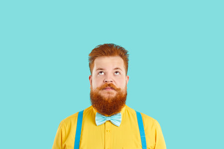 Funny redbeard Caucasian man carefully looks up at empty copy space and thinks and dreams about...