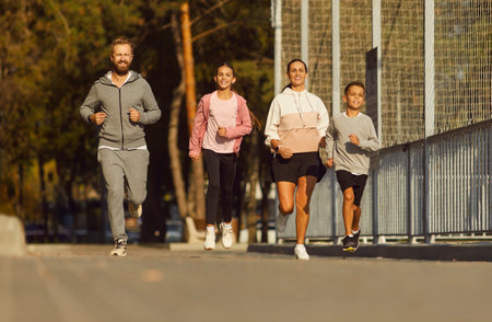 Happy fit family having outdoor jogging workout in city. Sporty healthy mum, dad and children in sportswear running together on urban street on sunny summer morning. Sport, fitness conceptの写真素材