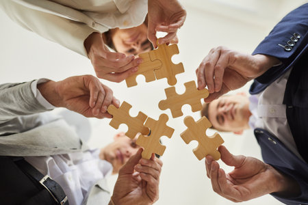 Bottom view of a confident business people putting together pieces of wooden puzzles. Caucasian colleagues join jigsaw pieces in the office. Cooperation, teamwork, help and support concept.の写真素材