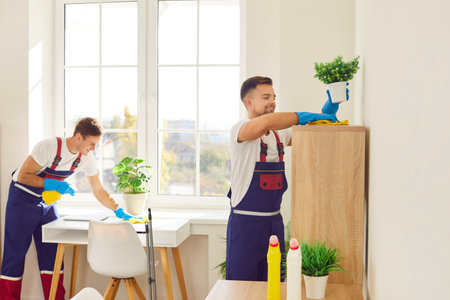 Professional cleaners working inside modern office or apartment. Two happy men from cleaning service...