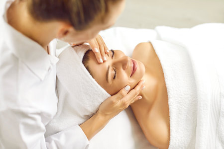 Close up portrait of a beautiful young woman lying with closed eyes and having face or head massage in spa. Woman relax enjoying health therapy treatment. Wellness and beauty day concept.の写真素材