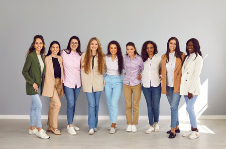 Full lenght portrait of a happy cheerfull young diverse group of women friends or coworkers and company employees looking at camera and smiling on grey wall background. Diversity, friendship concept.の写真素材
