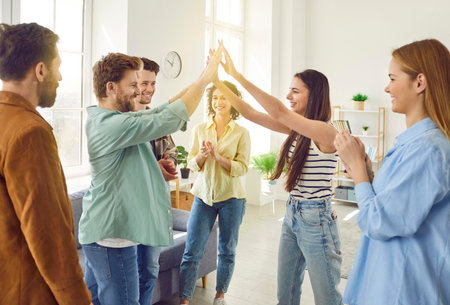 Portrait of a group of excited happy young friends students greeting each other giving high five when meet at home. Men and women standing in a circle enjoying time together at the party.の写真素材