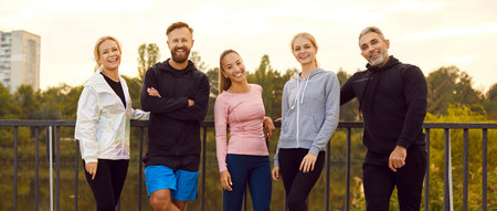 Portrait of a happy sporty people friends in sportswear looking at camera standing in a row on the bridge after successful workout in park. Outdoors training and fitness in nature concept. Banner.の写真素材
