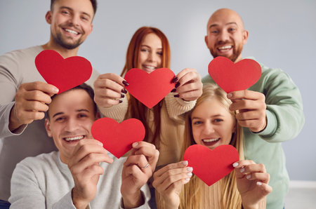Happy smiling group of young people friends holding paper red hearts in their hands celebrating valentines day together looking at camera isolated on gray background. Love and friendship concept.の写真素材