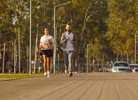 Young couple engages in a run in the city park. This jogging captures the synergy between the man and woman, showing the joy and togetherness found in their shared pursuit of fitness through training.の写真素材