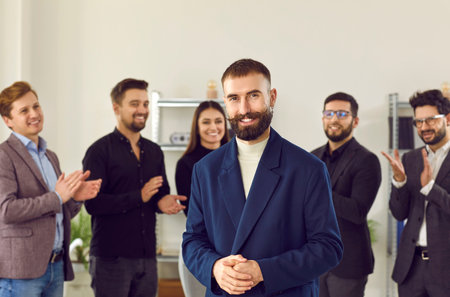 Smiling businessmen congratulate colleague on an achievement or promotion. Happy employees applaud an excited, beautiful, creative, well-groomed man in suit, welcome new team member at work.の写真素材