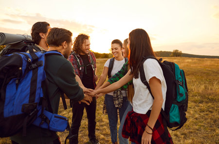 Team of happy tourists joining hands. Group of cheerful male and female friends with backpacks standing in autumn field, huddling and holding hands together. Tourism, hiking, leisure, teamwork conceptの写真素材