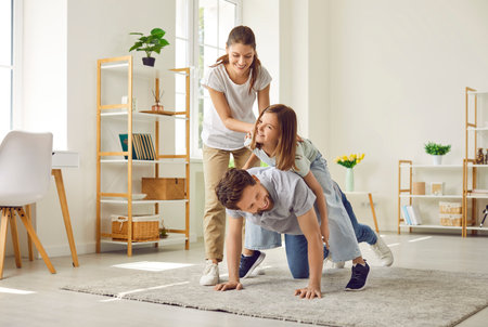 Happy laughing kid girl having fun with her family, sitting on fathers back at home. Portrait of young couple spending time and playing with their child daughter together. Family leisure concept.の写真素材