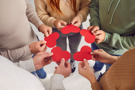 Group of friends exchanging valentines. Cropped shot of young adult people standing in circle and giving each other red heart shaped valentine cards. Love, care, affection, connection conceptの写真素材