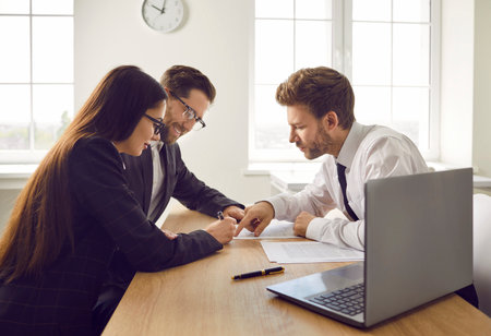 Portrait of young confident business woman sitting on workplace and signing a contract at office. Group of three coworkers and company employees make a good deal reaching agreement.の写真素材