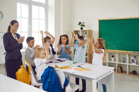 Happy friendly children and woman teacher together applaud student who coped with task best of all and rejoice at end school day stand . Elementary education, back to schoolの写真素材