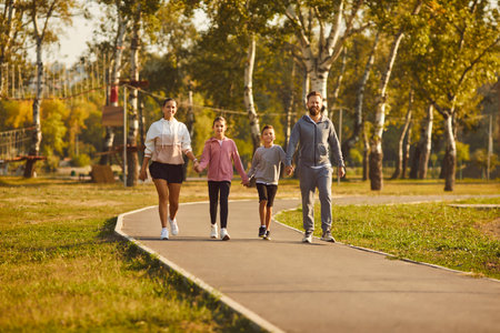 Sporty happy family with children wearing sportswear holding hands walking together in the park after sport workout outdoors. Healthy lifestyle, training and fitness in nature concept.の写真素材