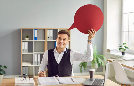 Young happy smiling businessman accountant wearing suit sitting in office on his workplace at the...