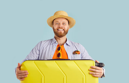 Young funny happy confident smiling man tourist in beach hat standing with his suitcase and going on...