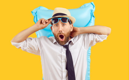 Funny bearded business man in office shirt, tie and summer holiday hat, with inflatable beach mattress, makes surprised open mouthed face when sees incredible sea view or very beautiful stunning womanの写真素材