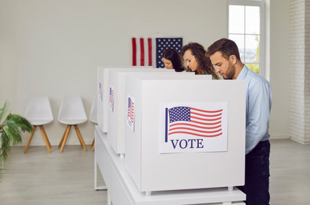 Group of USA citizens casts votes in booths during election day in a vote center office setting. The...