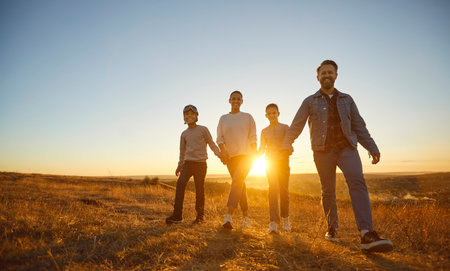Happy smiling family of four with two kids boy in pilots glasses and girl walking in the field together holding hands enjoying time together in nature at sunset time. Family leisure outdoors conceptの写真素材