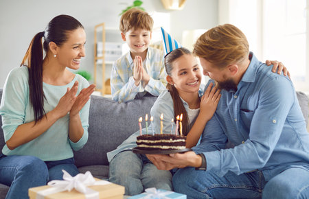 Happy girl celebrating birthday with family sitting on sofa in the living room at home. Smiling...