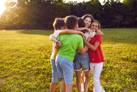 Carefree funny children pree-teens boys and girls in multi-colored T-shirts and shorts they all hug and frolic together enjoying sunbeams after walk with school friends be in summer parkの写真素材