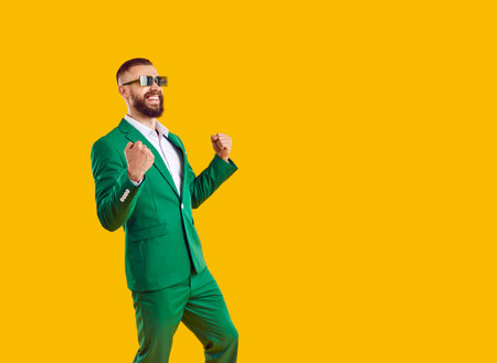 Overjoyed happy bearded showman businessman in green suit and sunglasses showing yes win gesture and...