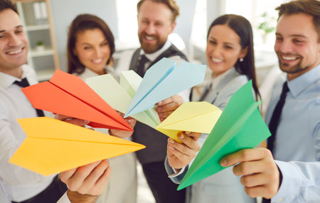 Top view of a group of happy people coworkers holding multicolored paper planes in hands planning...