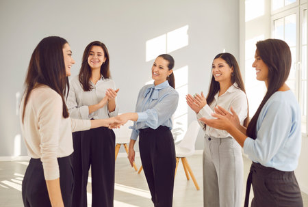 Happy women colleagues shaking hands on meeting in office, celebrating success, making a deal or business achievement. Female coworkers team applaud congratulating their partners on job well done.の写真素材