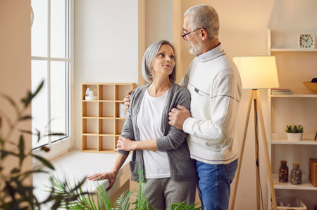 Portrait of aged senior couple hugging and smiling standing at home. Happy affectionate mature pair looking at each other enjoying being together. Romantic and relationship in retirement concept.の写真素材