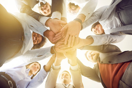 Group of diverse business professionals is shown from a low angle, standing in a circle and stacking...