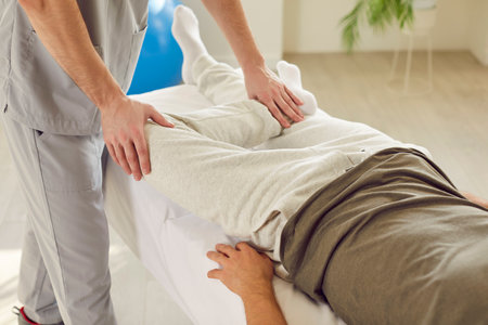 Close up of a caucasian man, therapist hands, massaging and stretching patient legs during a rehabilitation session in hospital office. Physical and physiotherapy aspects of the caregiver role.の写真素材