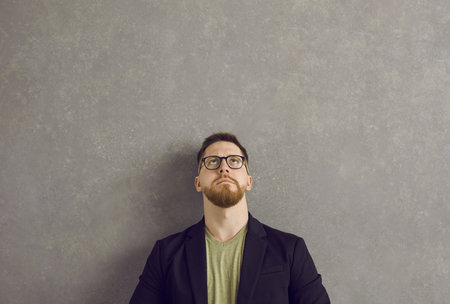 Serious caucasian man with a pensive and dubious expression looks up over his head. Millennial man...