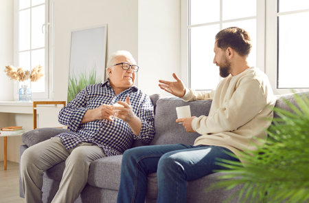 Familial connection family old father adult son sitting on sofa talking happy fatherhood. Family connection father and son heartwarming fatherhood bond between generations Happy fatherhoodの写真素材