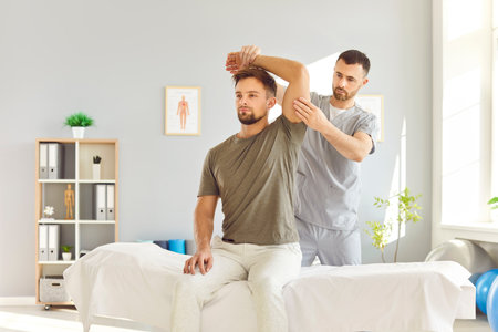 Caucasian male physiotherapist is providing massage and arm stretching therapy to a patient during healthcare rehabilitation. Recovery medical exercises in physical therapy sessions.の写真素材