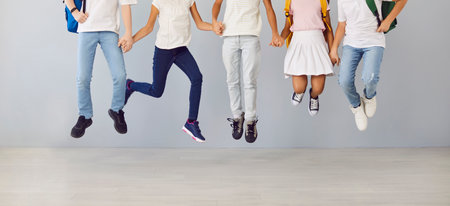 Cropped photo of legs of school students children jumping isolated on gray wall background. Boys and girls wearing casual clothes holding hands in a row. Back to school concept. Banner.の写真素材