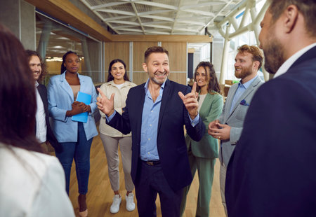 Boss or business coach, stands with a beaming smile at the center of a circle, surrounded by team members during an office meeting. Convey collaborative leadership and effective communication.の写真素材