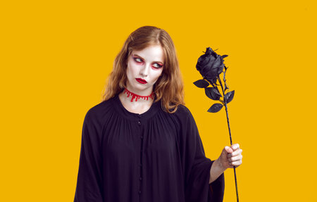 Portrait of mysterious scary dead woman with black rose in her hand on orange background. Witch...