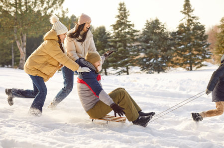 Happy family having fun sledding their smiling father together in winter park. Young parents with two children walking together outdoors in forest. Family leisure and winter holidays concept.の写真素材