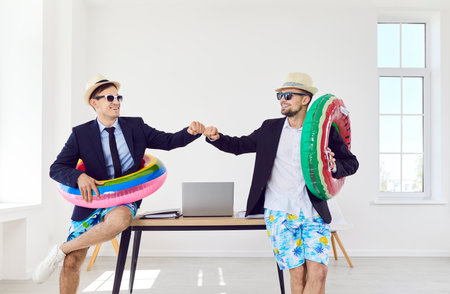 Funny business male workers in sunglasses and beach hats standing at desk in office with rubber ring going on holiday trip and ready for summer vacation. Travel, journey and travelling concept.の写真素材