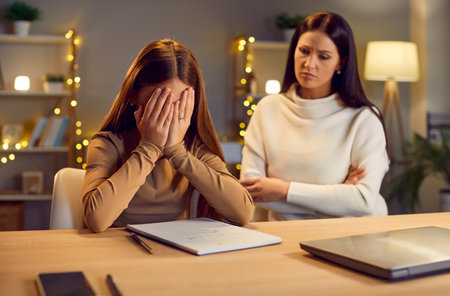Mother sits together with crying young daughter, who doing homework at evening home. Sadness and frustration, the mother provides support, assistance and comforting in education process.の写真素材