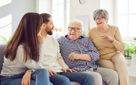 Happy Caucasian elderly parents and adult children sit together on the sofa at home, talking and...