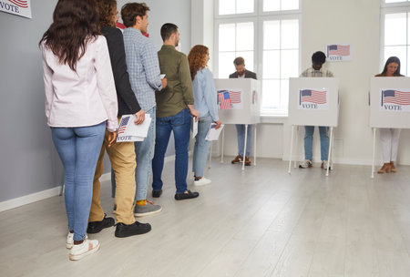 USA citizens line up to exercise right to vote. The election day fervor is palpable at the vote center office, where voters await their turn to enter the voting booths adorned with American flags.の写真素材