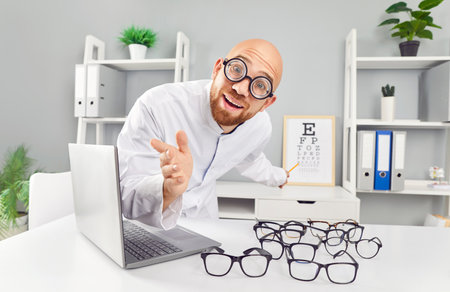 Portrait of happy smiling funny male ophthalmologist sitting in his office at the desk checking a patients vision. Man doctor looking at camera in clinic. Ophthalmology, eye health concept.の写真素材