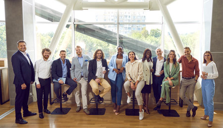 Team of happy diverse people meeting at professional business event. Group portrait smiling young senior multiethnic men and women in smart casual wear in modern office interior with big glass windowの写真素材