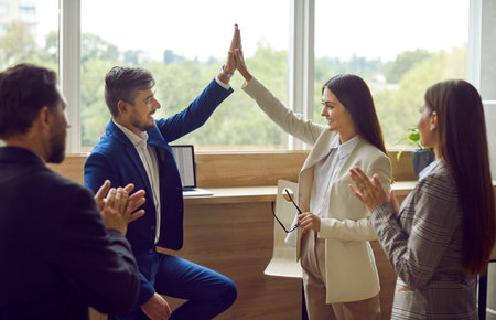 Happy colleagues man and woman giving high five at meeting at the office, celebrating success, making a deal or business achievement. Coworkers applaud congratulating their partners on job well done.の写真素材